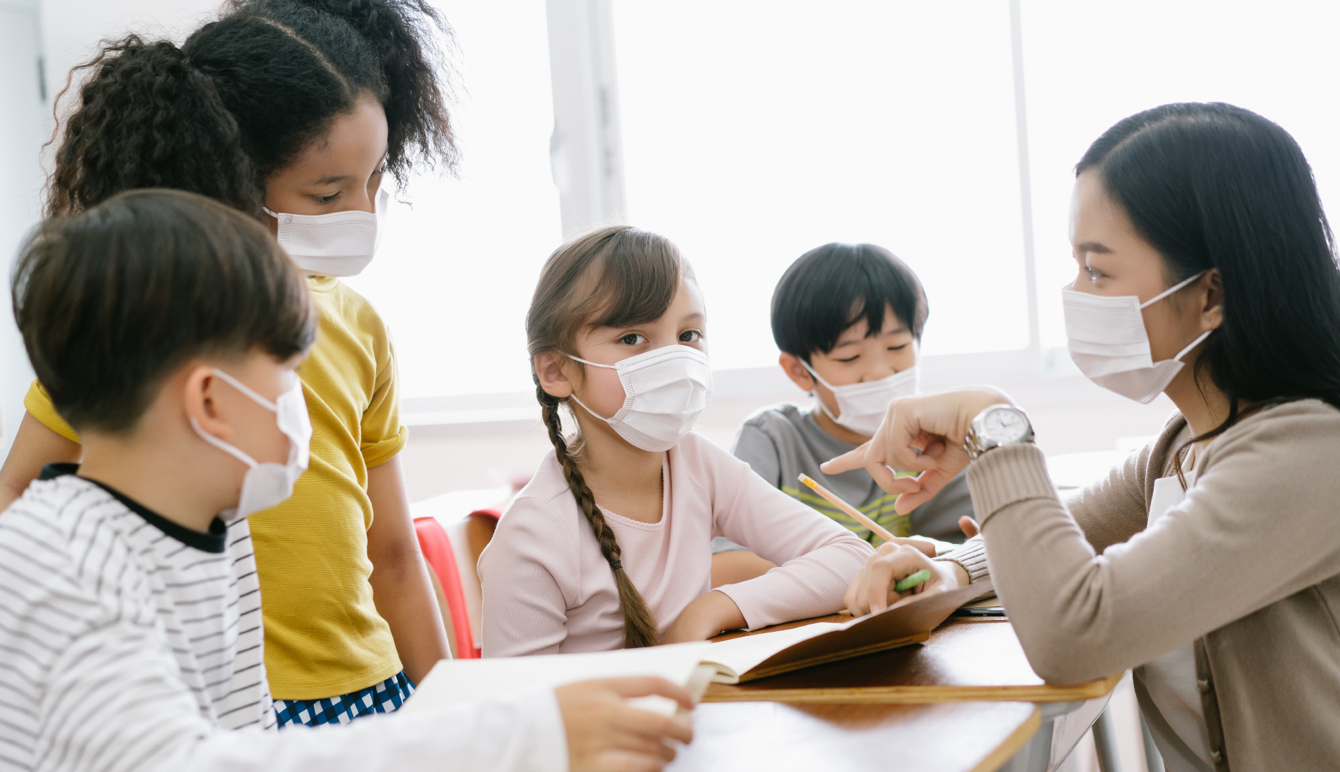 A teacher works with her students, all wearing face masks