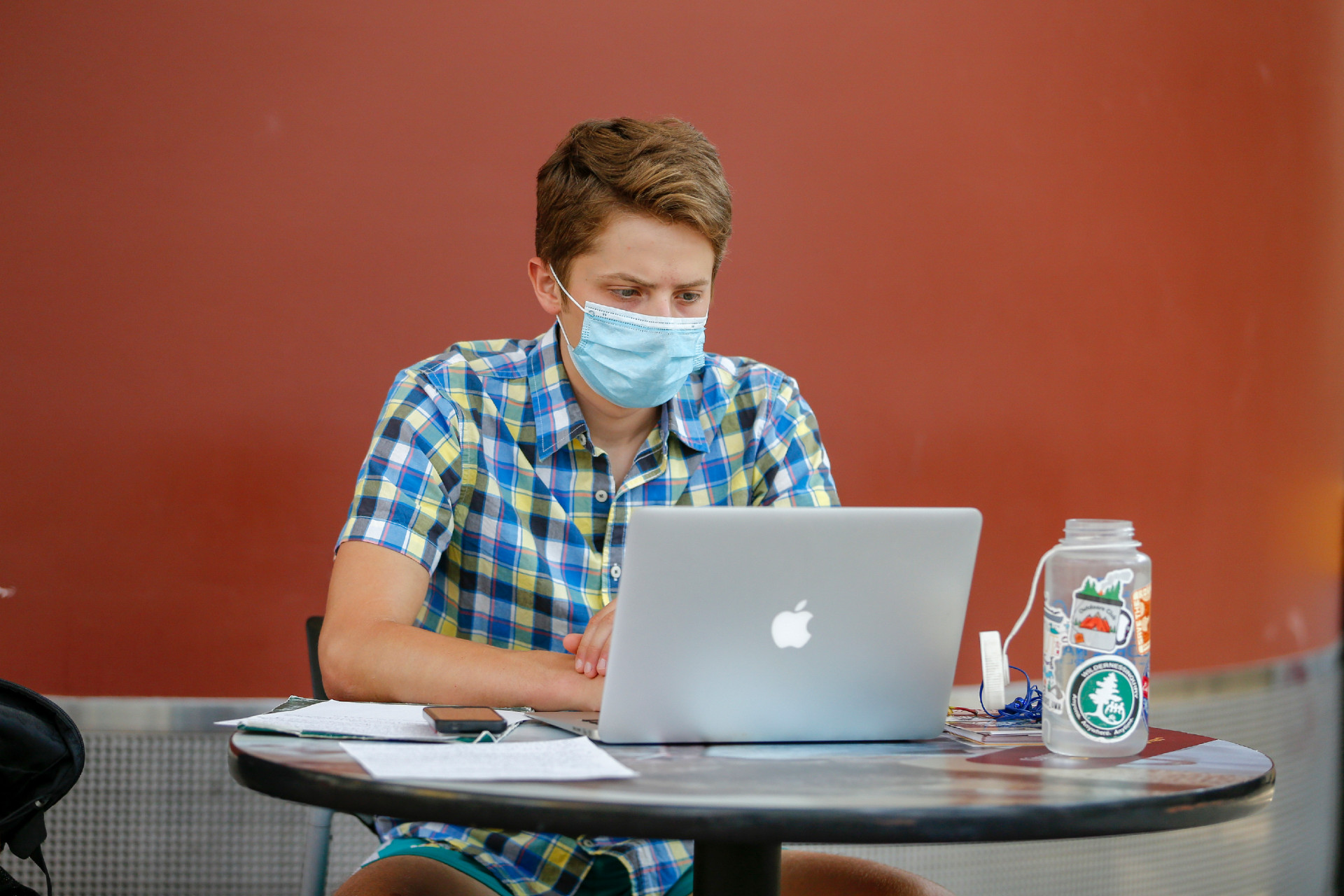 A student works on his computer while wearing a mask